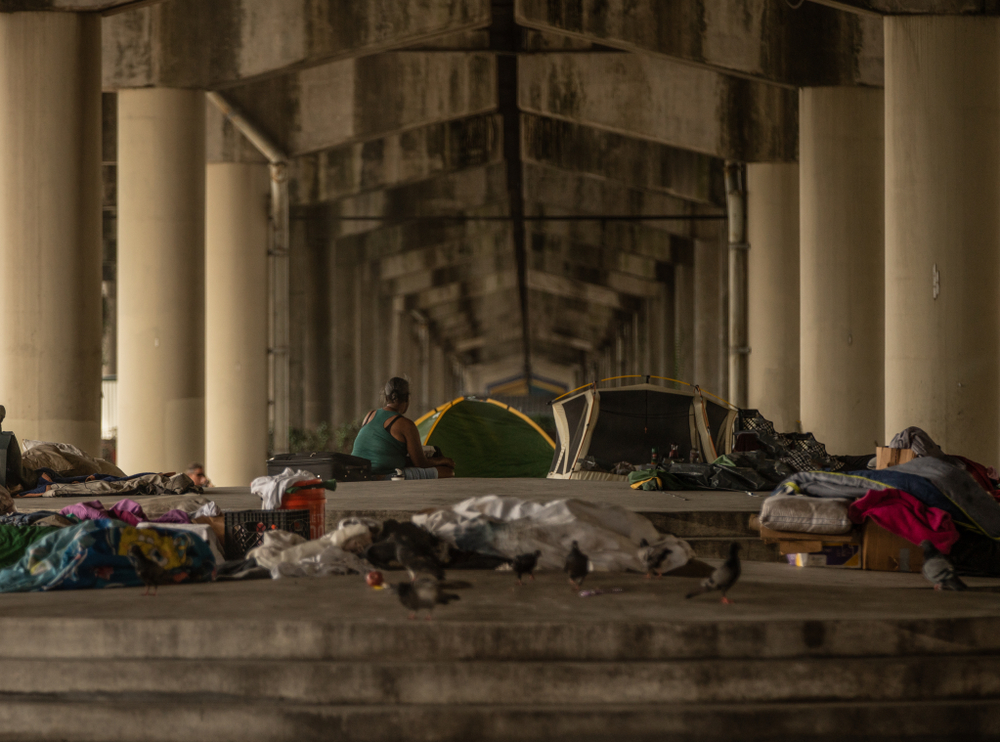 Woman sitting with tents under bridge.