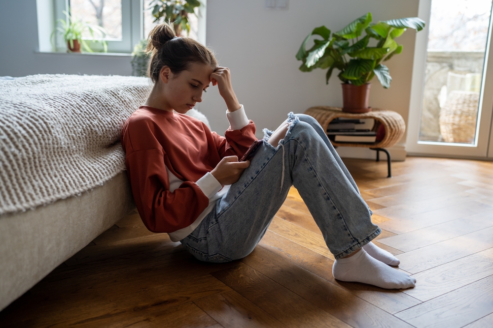 Young woman sitting on bedroom floor looking at cellphone.